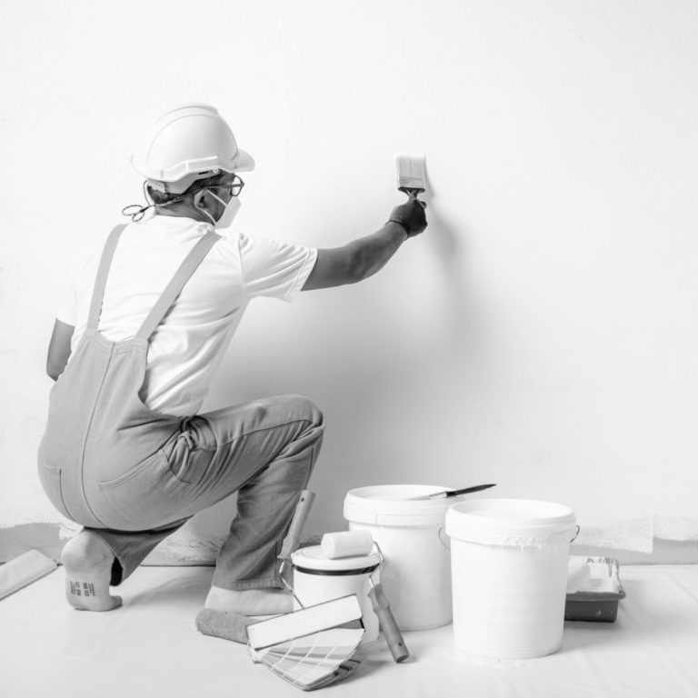 Maler streicht eine weiße Wand Mann streicht eine weiße Wand, umgeben von Farbeimern und Werkzeug.