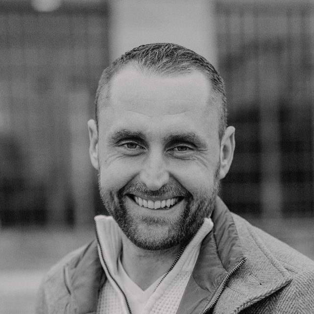 Brian Krüger mit kurzem Haar, trägt einen grauen Pullover und steht im Freien.