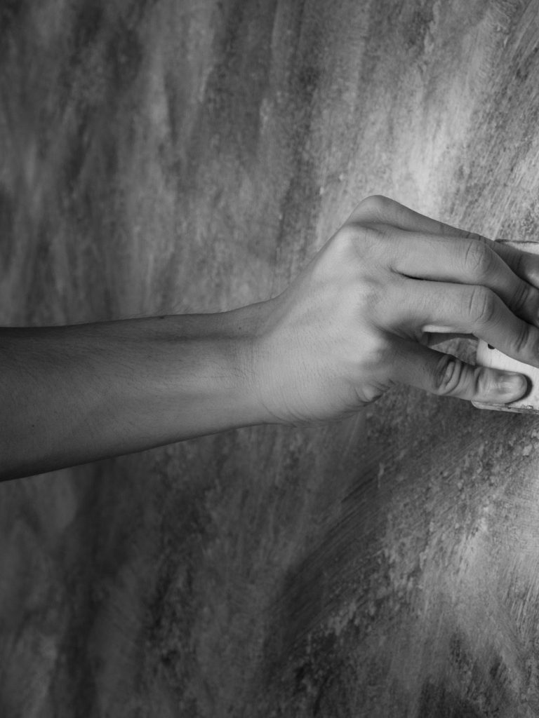 erster Teil Bild Wandbemalung mit Pinsel Eine Hand wischt mit einem Pinsel über eine wandartige Oberfläche.