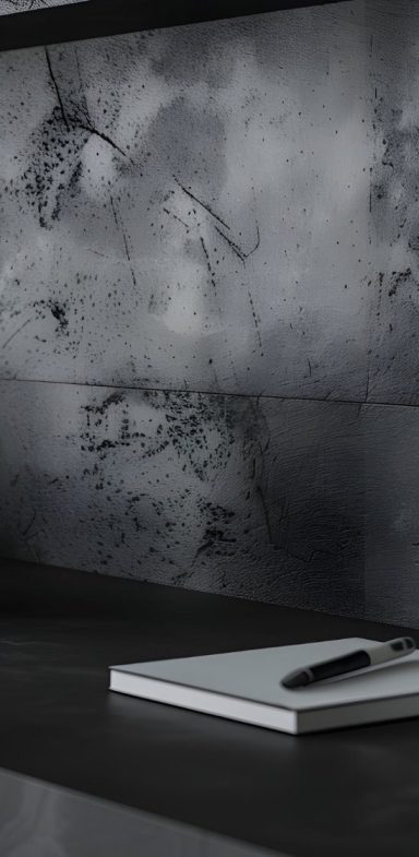 Schlichte Arbeitsfläche mit einem Notizbuch und Stift vor einer grauen Wand.