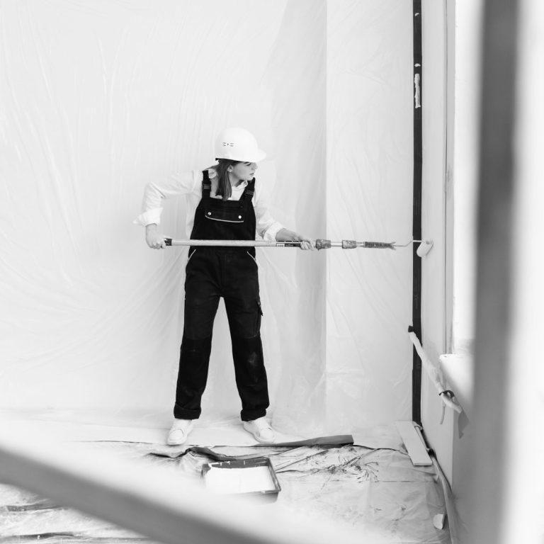 Malerin bei der Arbeit Arbeiter in Schutzkleidung streicht eine Wand in einem leeren Raum.