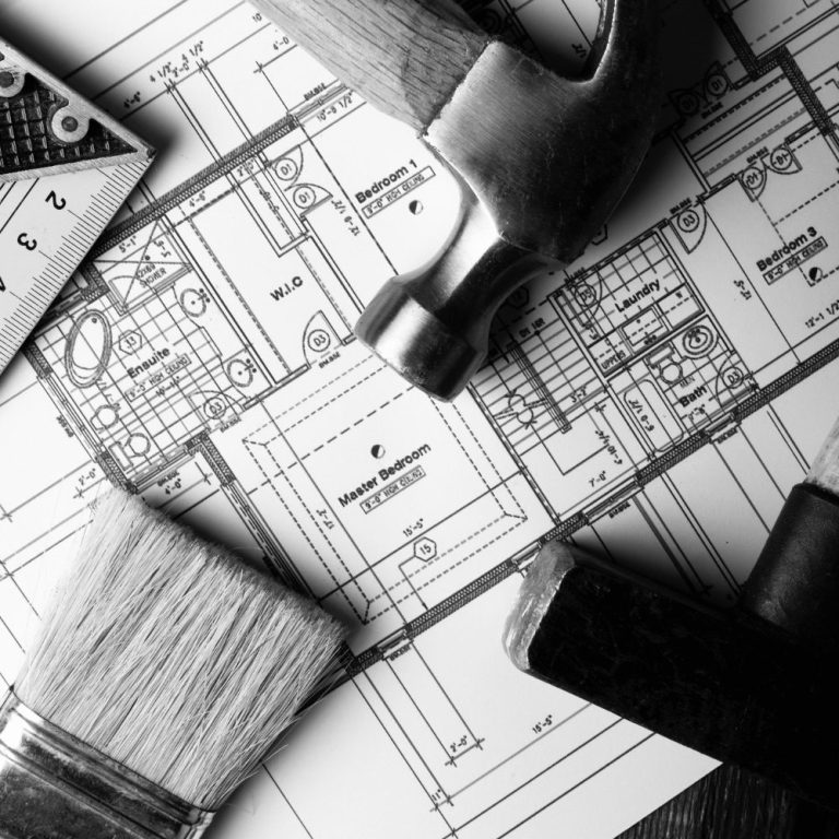 Baupläne und Werkzeuge wie Hammer und Pinsel auf einem Tisch angeordnet.