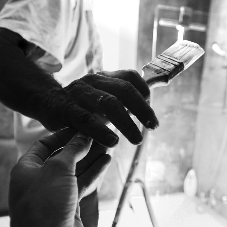 Eine Hand reicht einen Pinsel, während die andere Hand ihn greift. Schwarz-Weiß Aufnahme.