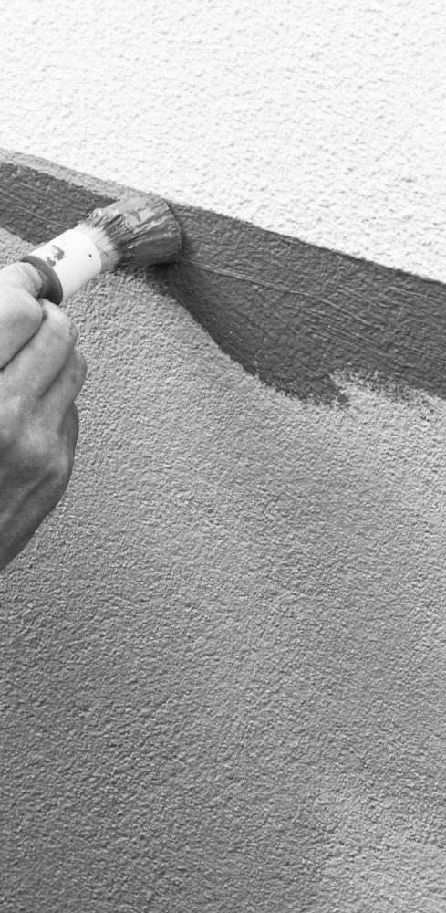 Brian Krüger bei der Arbeit Eine Hand, die mit einem Pinsel eine Wand in verschiedenen Grautönen streicht.