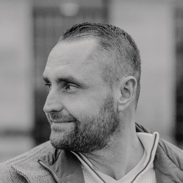 Brian Krüger im Profil Ein Mann mit kurzem Haarschnitt und Bart, der lächelnd zur Seite schaut. Der Inhaber Brian Krüger