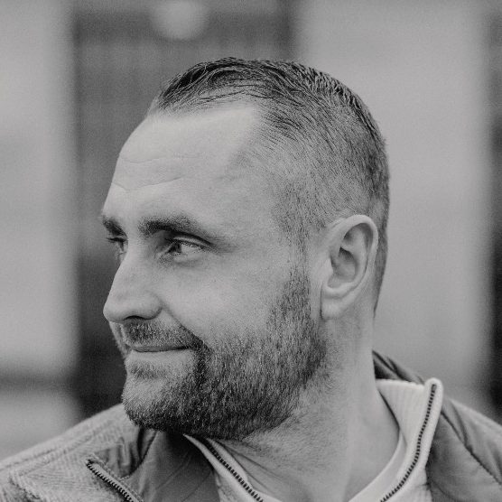 Brian Krüger - Inhaber Lächelnder Brian Krüger mit kurzem Haar und Bart, blickt zur Seite.