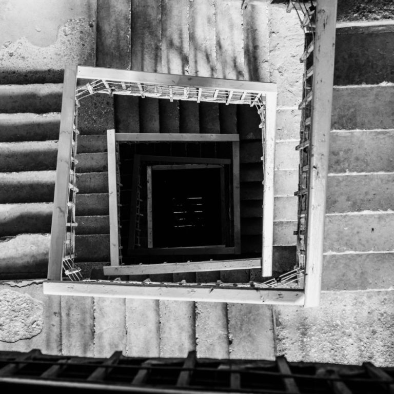 Schwarz-weiß Foto einer spiraligen Treppe, von oben nach unten aufgenommen.