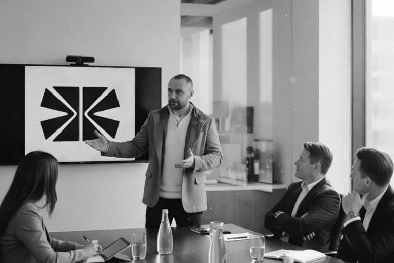 Brian Krüger präsentiert sein Konzept Brian Krüger präsentiert in einem Konferenzraum eine Grafik vor drei Zuhörern.