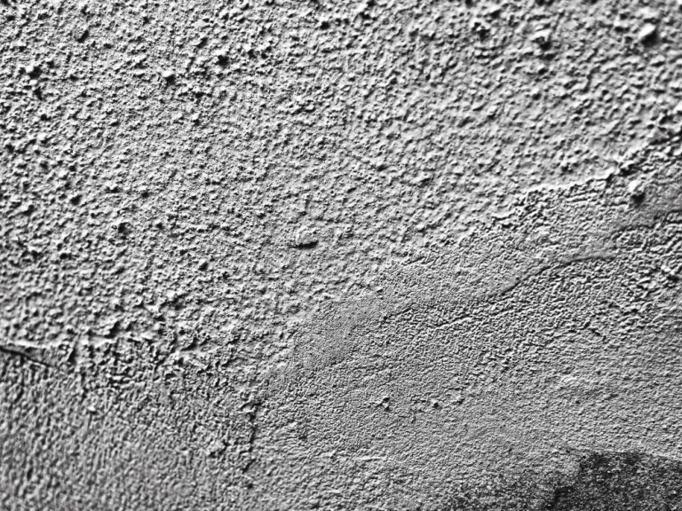 Verputzte Wand Rauhe, graue Wandoberfläche mit unregelmäßigen Strukturen und Zeichen.