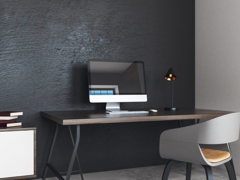 Moderne Schreibtischecke mit Computer, Lampe und Stuhl vor schwarzer Wand.