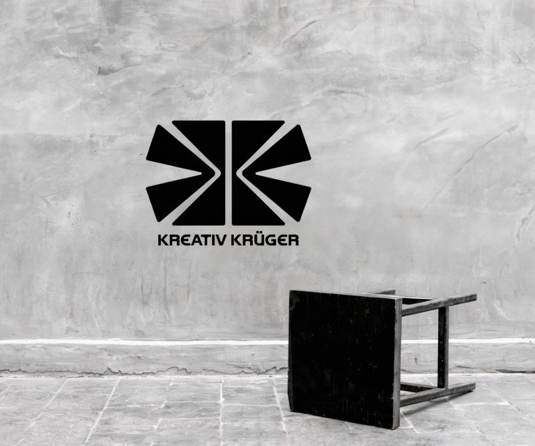 Schwarzer Stuhl vor grauer Wand mit schwarzem Logo "Kreativ Kröger".