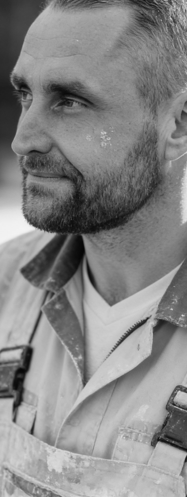 Brain Krüger der Inhaber Ein Mann mit Bart (der Inhaber), in Arbeitskleidung, schaut nachdenklich zur Seite.