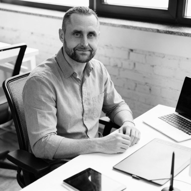 Brian Krüger sitzt an einem Schreibtisch mit Laptop und notiert etwas.